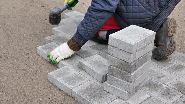 Hands of a worker installing concrete blocks, paving slabs with a rubber hammer