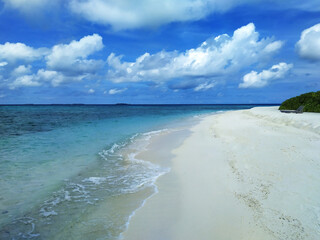 Maldives, the deserted beach with white sand. The turquoise ocean and blue sky with clouds.