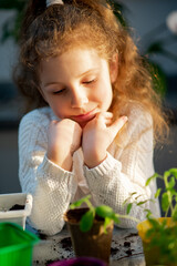 A cute girl plants at home in eco pots. She is wearing a white sweater. The garden of the house. Hobby.