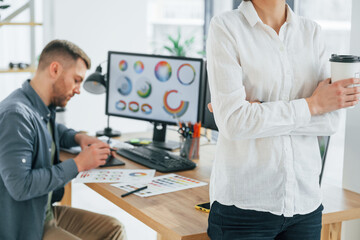 Woman standing in front of man that sitting by the table. Two designers working together in the office