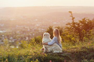 Fototapeta na wymiar Blonde woman and golden retriever sitting on the hill at sunset.