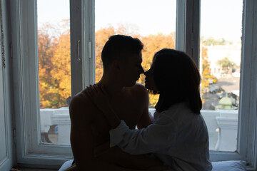 Man and woman sitting on the windowsill in front of the big window in the bedroom. Concept of love.