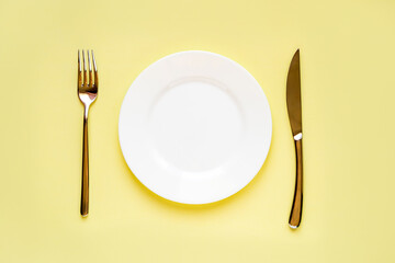 white empty plate and cutlery knife and fork on yellow background