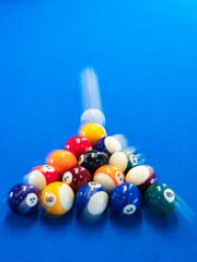 Blurry of colorful balls on a blue billiard table. Beginning of game, slow motion, soft focus. Indoor leisure, entertainment, hobby and sport concept. Cue ball moving away after the pool break.