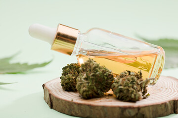 Glass dispenser bottle with extract marijuana oil, with green cannabis buds and leaves. green background