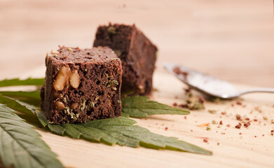 marijuana brownie on marijuana leaves, dessert on wooden table.