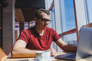 Smart software developer sitting at desktop in coworking space with laptop and creating publishing idea, using netbook for messaging and networking during freelance work