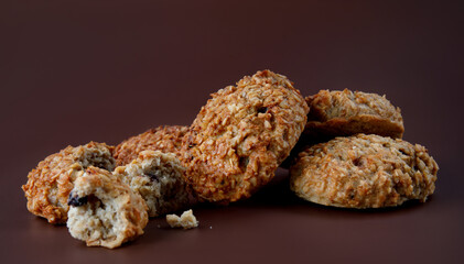 Whole and crushed handmade oatmeal cookies on a brown background.