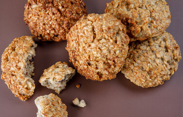 Whole and crushed handmade oatmeal cookies on a brown background. View from above .