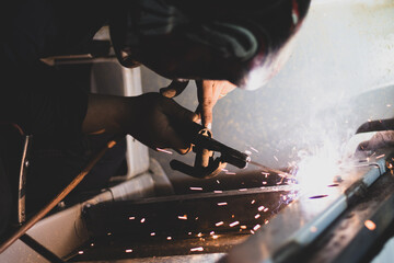 Closeup shot of a  metal fabricator making an automotive welding with flames in a car factory