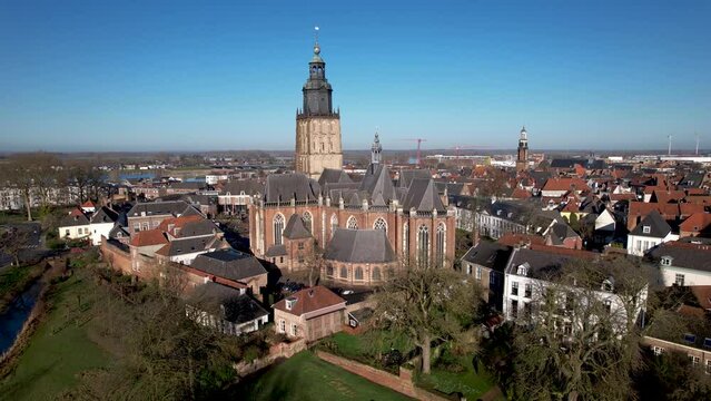 Panning movement showing medieval city surrounding Walburgiskerk cathedral with various rooftops and part of original city wall in the foreground on a bright sunny day against a clear blue sky