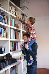 I want that one at the top. A young boy sitting on his dads shoulders to reach a book in their book...