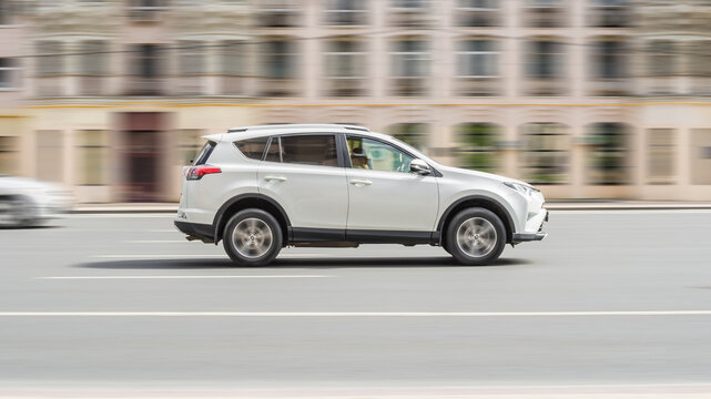 White Toyota RAV4 car is moving fast along the street with blurred urban background