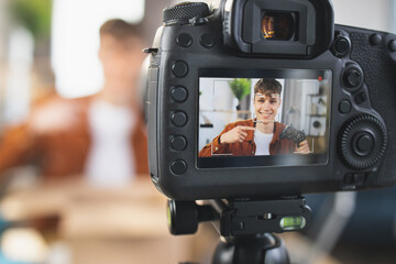 Close up of modern camera screen with smiling man sitting at desk and opening box with joystick. Focus on video camera. Concept of purchases, blogging and delivery.