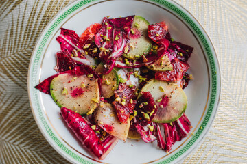 radicchio salad with watermelon radish, blood orange, pistachios on white plate with green greek key