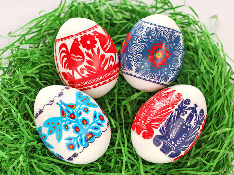Four Colourful Easter Eggs with floral, birds, people folk art pattern printed on stickers. Eggs in green paper grass nest. Polish traditional paper-cut from Kurpie region - Wycinanka Kurpiowska.