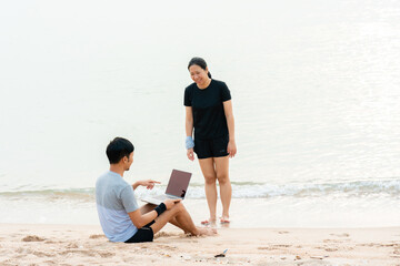 The young couple were chatting to their colleagues via video, on their laptop computers, on the sandy beach where the slow waves crashed against the shore, happily and comfortably.