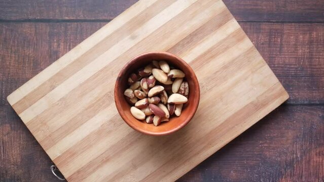 top view of Brazilian nut dropping in a bowl on wooden background 