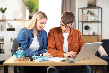 Students, man and woman in casual outfit using laptop during working together. Young business partners cooperating at bright office or working online from home