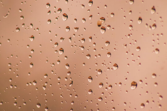 Petites gouttes d'eau de pluie sur vitre de verre couleur champagne.