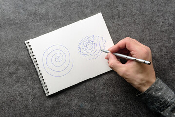 A man with trembling hands is trying to repeat the spiral drawing in a notebook. Test for essential tremor and parkinson's disease. - obrazy, fototapety, plakaty