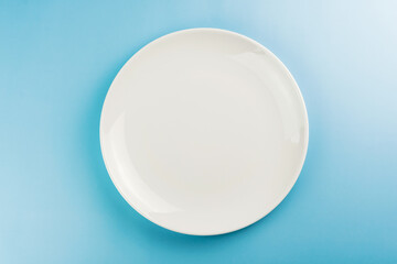 Empty white plate on the blue table. Top view. Space for text