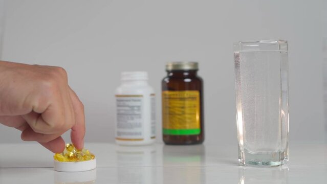 A hand takes a fish oil capsule from the table and drinks it down with water.