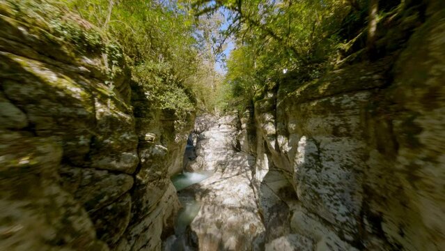 FPV drone extreme shot flying over natural canyon cliff formation with tropical plant greenery woodland cascade landscape. Aerial view fast movement cold splashing water with stones jungle rocky creek