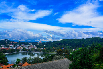 Sky with white clouds and a village with a lake surrounded by greenery