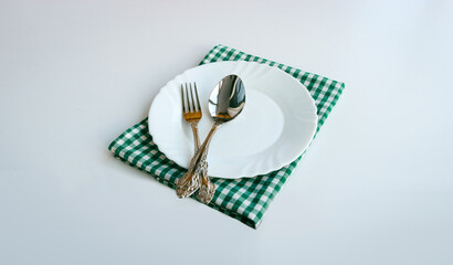 White plate, cutlery and checkered doily on a light background.