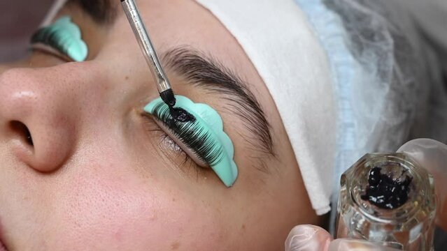 Young woman undergoing eyelash tinting and lamination procedure.