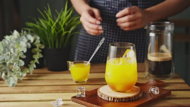 Iced black coffee with orange Juice. Cold coffee with tonic. The barista mixes ice cubes, Juice, orange syrup and cold coffee. 