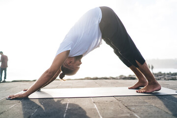 Flexible male in sportswear have yoga training at embankment spending daytime for reaching vitality wellness, Caucasian man recreating during morning stretching at black mat keeping healthy lifestyle