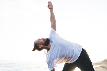 Concentrated male yogi stretching and training during pastime at coastline spending weekend for...