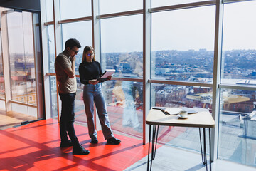 A young business woman with documents in glasses stands with a male manager while holding a corporate business meeting in a modern office. Business meeting concept. Free space, selective focus