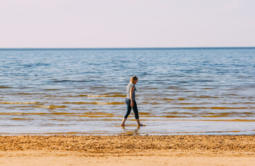 Fototapeta na wymiar Teenager girl walks on the sea coast. Barefoot girl on a sandy beach. 