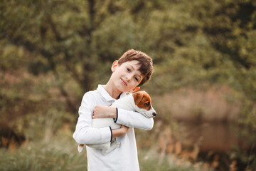 Outdoor portrait of a boy gently hugging a jack russell terrier puppy. Child loving and caring for a pet, friendship with animals