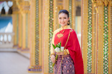 Fototapeta premium Attractive Thai woman in an ancient Thai dress holds a fresh flowers paying homage to Buddha to make a wish on the traditional Songkran festival in Thailand