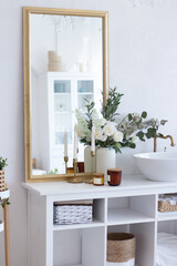 Beautiful bathroom interior. Large mirror in a golden frame, white shell, white flowers, candles, green flowers. Organization of space in the bathroom.