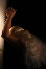 Vertical shot of an emotional Caucasian woman posing near the blinds in a dark room