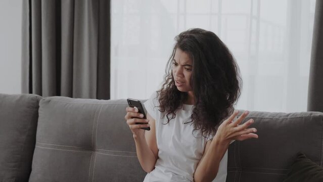 Young African American lady shocked and frustrated looking at phone seeing bad news photos text message with disappoitment and anxiety emotion on face