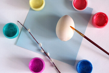 Wooden egg with a brush, colorful paints (yellow, green, blue, red and pink) and willow, verba branch. Top view. Easter preparation concept background. Spring holidays gifts. Creativity, DIY