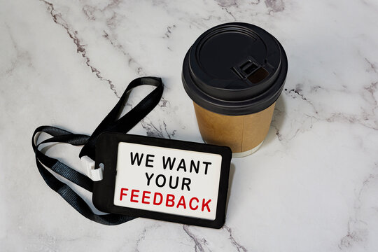 We Want Your Feedback On Black Name Tag With Disposable Coffee Cup On White Desk