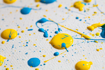 Blue and yellow paint drops on white canvas.