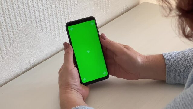 Smartphone green screen. Close-up of the hands of an elderly woman using a chromakey smartphone reads news on a mobile phone, communicates on social networks, communicates with friends.