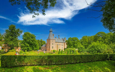 View over green garden park hedge on medieval dutch water castle from 14th century with green trees, clear blue summer sky - Doorwerth, Kasteel, Netherlands