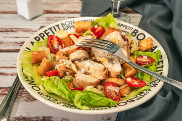 Exquisite variation of Caesar salad with thin slices of chicken, cherry tomatoes and a gourmet aioli sauce in a small bowl on a rustic table. Gourmet concept.