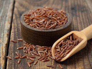 Red rice in a wooden scoop on a dark wooden rustic background