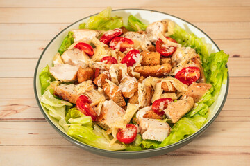 Exquisite variation of Caesar salad with small bites of chicken, cherry tomatoes and a gourmet aioli sauce in a small bowl on a table. High view.