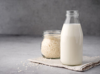 Vegan rice milk with rice grains on a gray concrete background. Copy space. Non dairy alternative milk. The concept of healthy vegetarian food and drinks. Diet healthy concept. Gluten-free breakfast.